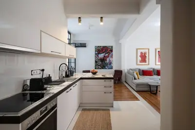 a kitchen with white cabinets and a living room at Ebullience - Stylish & Chic Athens Apartment in Athens